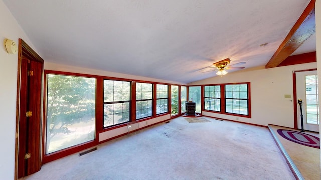 unfurnished sunroom featuring a wood stove, ceiling fan, vaulted ceiling with beams, and a wealth of natural light