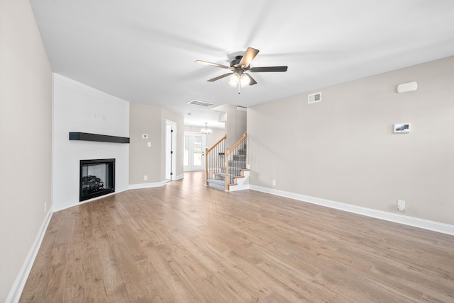 unfurnished living room with ceiling fan with notable chandelier, light hardwood / wood-style floors, and a fireplace