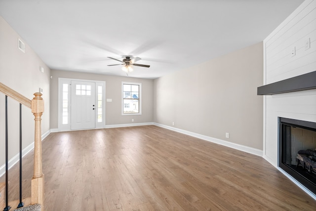 unfurnished living room with hardwood / wood-style flooring, a large fireplace, and ceiling fan