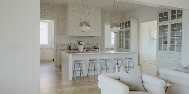 kitchen featuring decorative light fixtures, white cabinetry, backsplash, a kitchen bar, and light hardwood / wood-style flooring