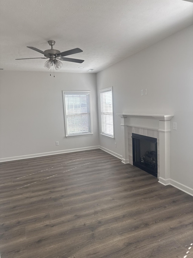 unfurnished living room featuring a tiled fireplace, ceiling fan, and dark hardwood / wood-style floors