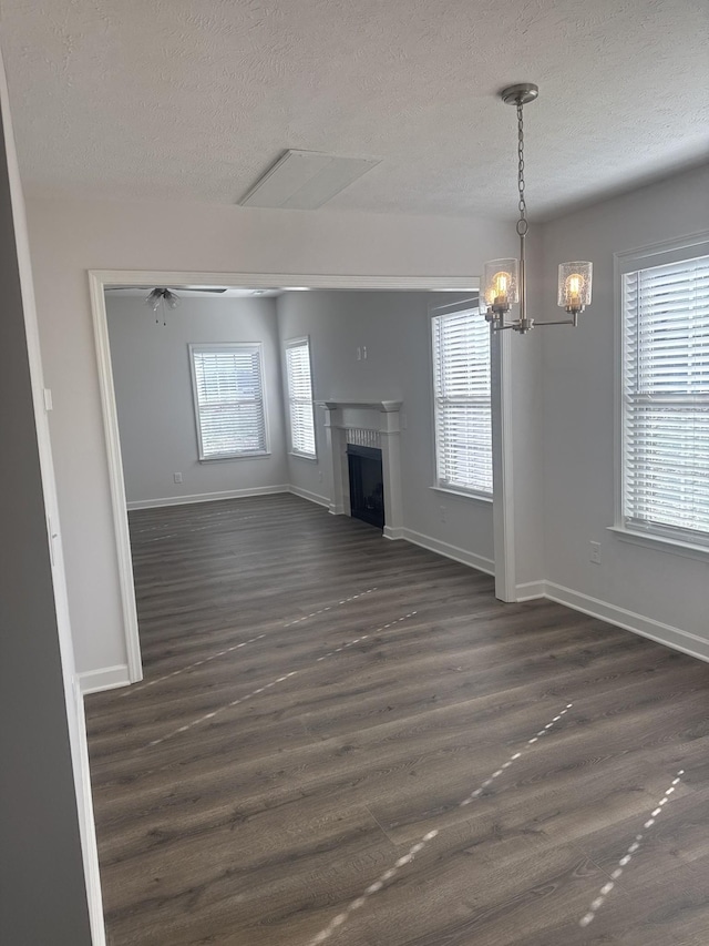 unfurnished living room with ceiling fan with notable chandelier, a textured ceiling, and dark hardwood / wood-style floors