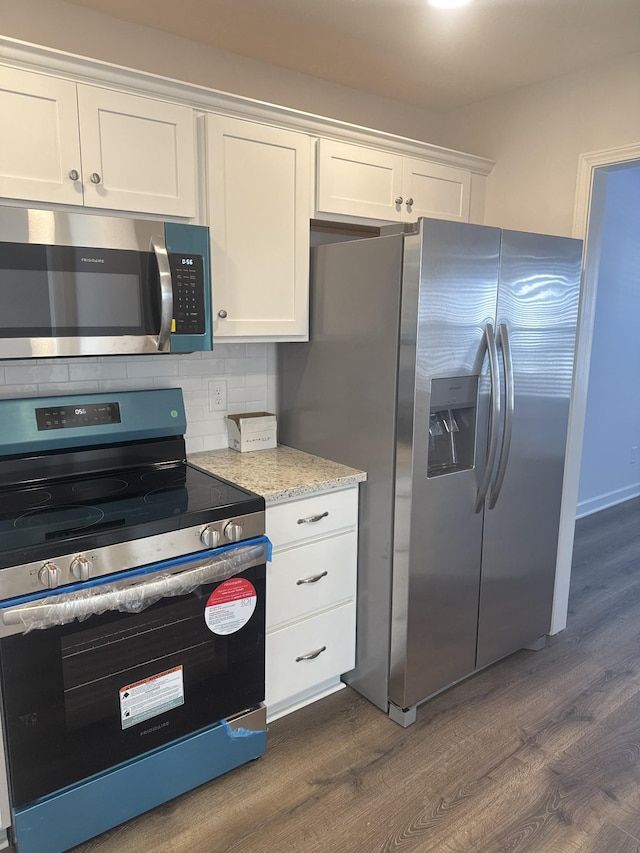 kitchen with light stone countertops, dark hardwood / wood-style floors, stainless steel appliances, backsplash, and white cabinetry