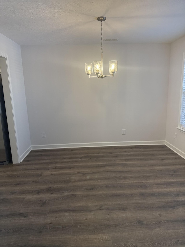 unfurnished room with a textured ceiling, dark wood-type flooring, and an inviting chandelier