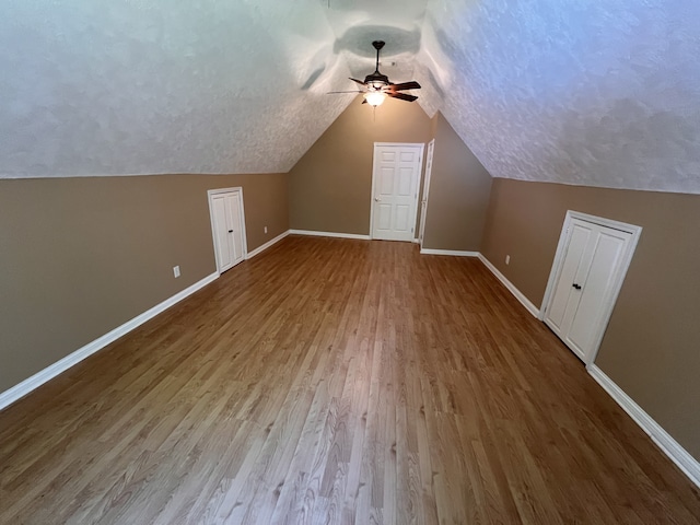 additional living space featuring a textured ceiling, wood-type flooring, ceiling fan, and vaulted ceiling