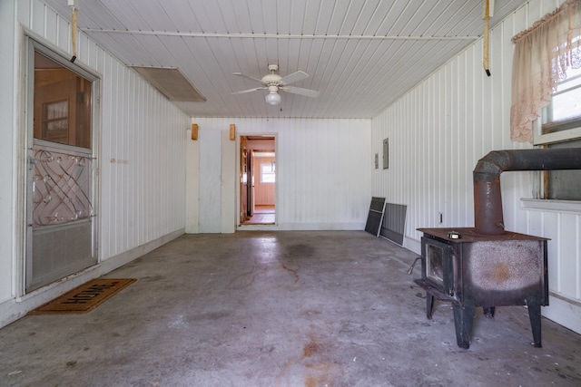 interior space featuring ceiling fan, concrete floors, and a wood stove