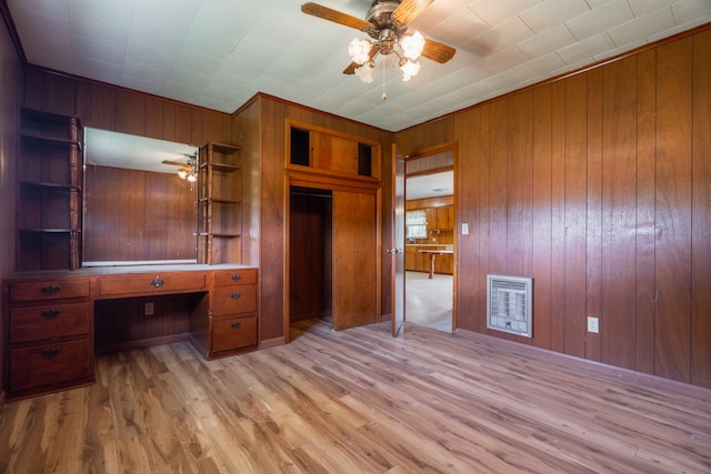 unfurnished bedroom featuring ceiling fan, built in desk, wood walls, and light hardwood / wood-style flooring