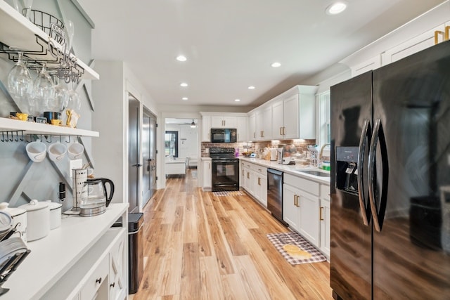 kitchen with light hardwood / wood-style flooring, backsplash, black appliances, white cabinets, and sink