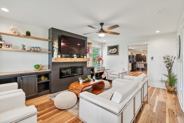 living room with ceiling fan, light hardwood / wood-style floors, and a large fireplace