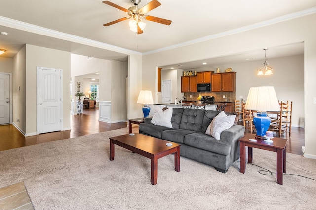 living room with ornamental molding, ceiling fan, light wood finished floors, and baseboards