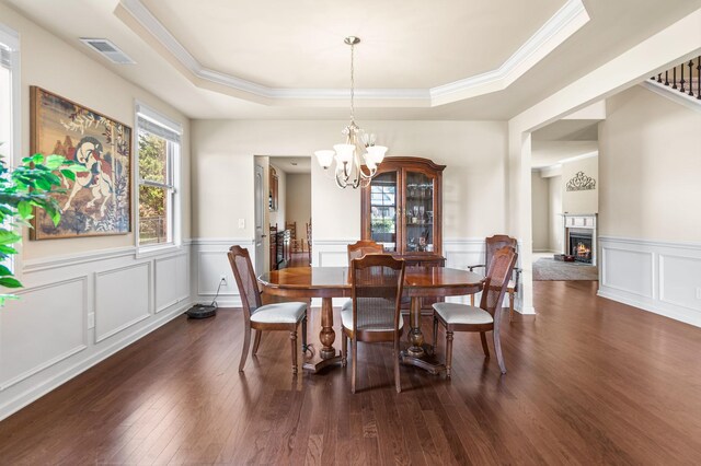 dining space with a warm lit fireplace, a notable chandelier, wood finished floors, visible vents, and a raised ceiling