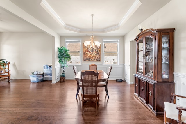 dining room with a notable chandelier, dark wood-type flooring, ornamental molding, and a tray ceiling