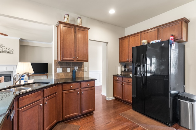 kitchen featuring decorative backsplash, dark wood-type flooring, dark stone countertops, black refrigerator with ice dispenser, and sink