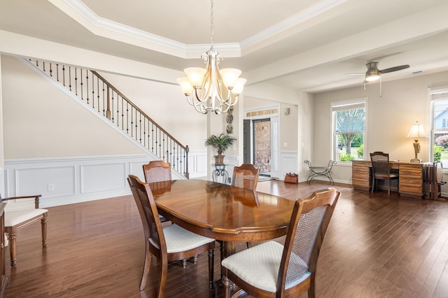 dining space featuring a decorative wall, ceiling fan with notable chandelier, stairs, dark wood-style floors, and a raised ceiling