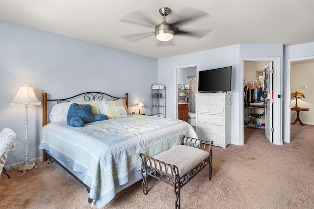 bedroom featuring ceiling fan, connected bathroom, a walk in closet, and light colored carpet