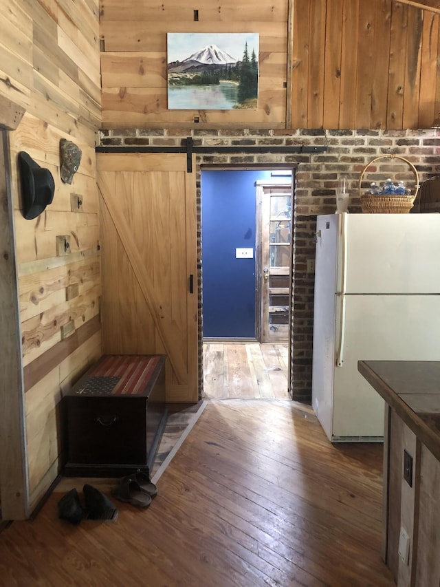 kitchen with a barn door, wooden walls, white fridge, and wood-type flooring