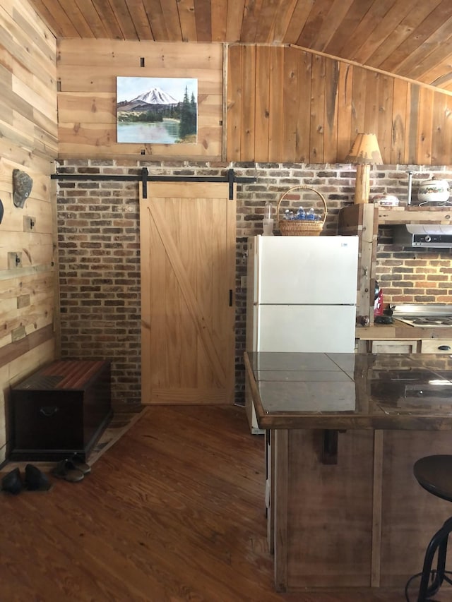 kitchen with vaulted ceiling, a barn door, wooden ceiling, dark hardwood / wood-style floors, and wood walls