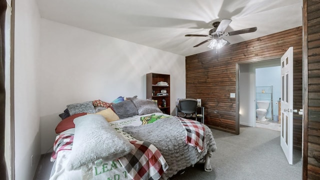 carpeted bedroom featuring ensuite bath, ceiling fan, and wooden walls