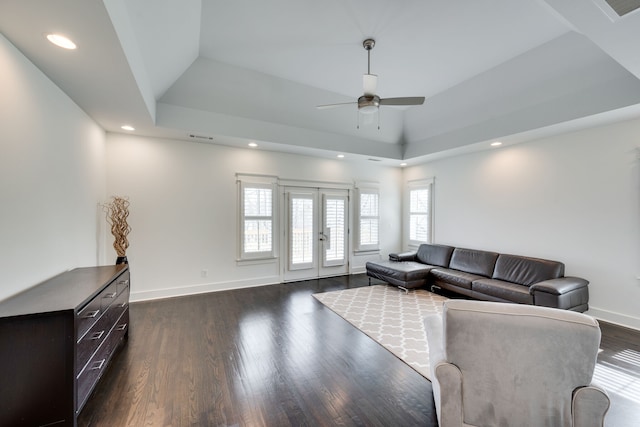 living room featuring dark hardwood / wood-style floors, a tray ceiling, ceiling fan, and a healthy amount of sunlight