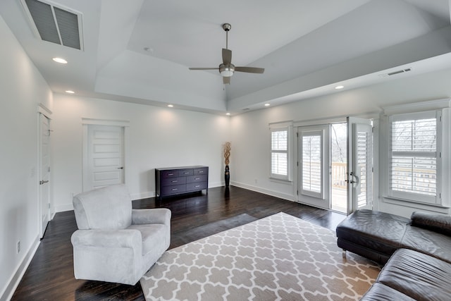 living room featuring ceiling fan, a tray ceiling, and dark wood-type flooring