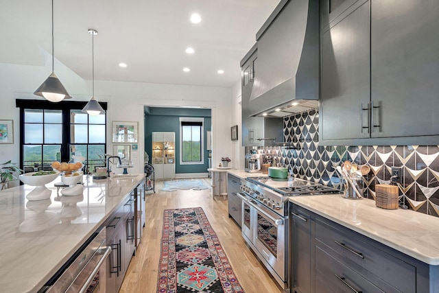 kitchen featuring premium range hood, light stone counters, decorative backsplash, decorative light fixtures, and range with two ovens