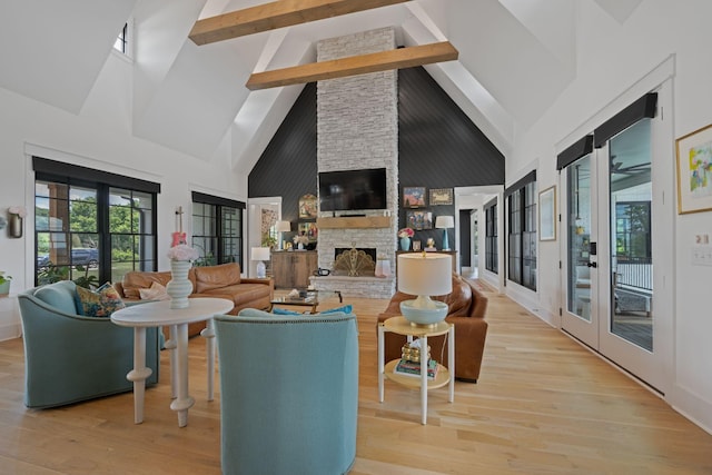 living room featuring light hardwood / wood-style flooring, beam ceiling, high vaulted ceiling, a stone fireplace, and french doors