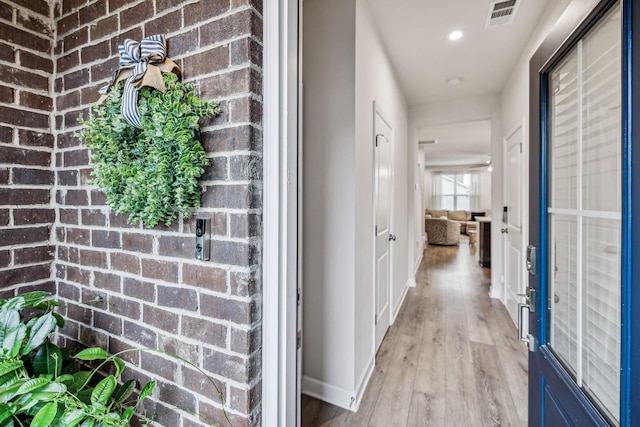 hallway featuring light wood-type flooring and brick wall