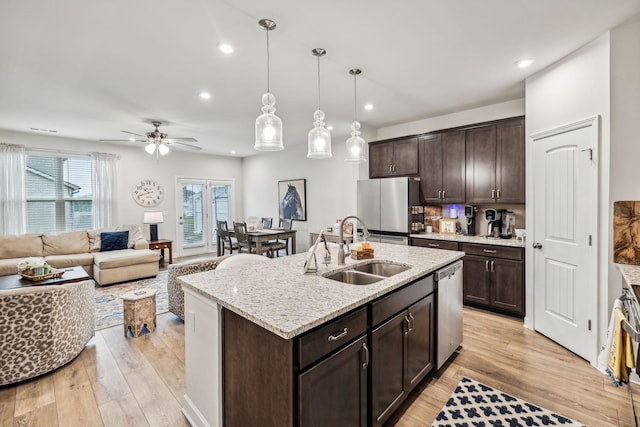 kitchen with sink, stainless steel appliances, light hardwood / wood-style flooring, decorative light fixtures, and a center island with sink