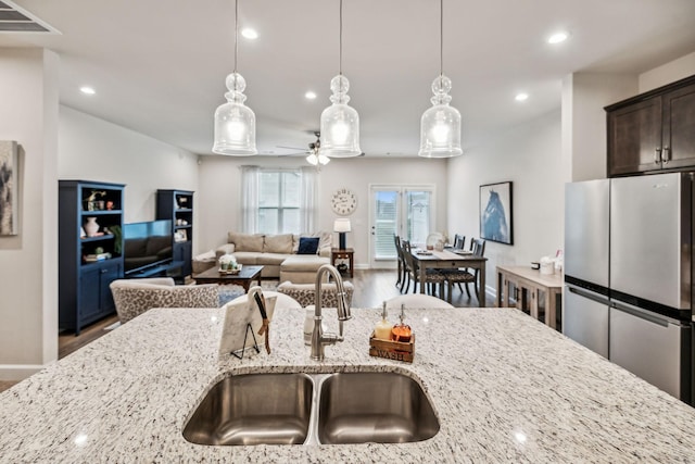 kitchen with stainless steel fridge, light stone counters, sink, and hanging light fixtures