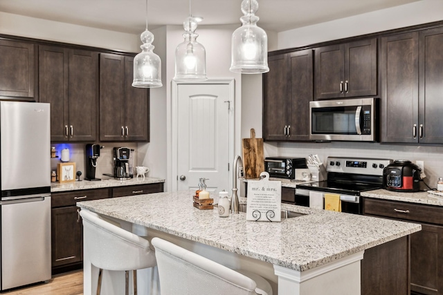 kitchen with a center island with sink, decorative light fixtures, tasteful backsplash, dark brown cabinets, and stainless steel appliances