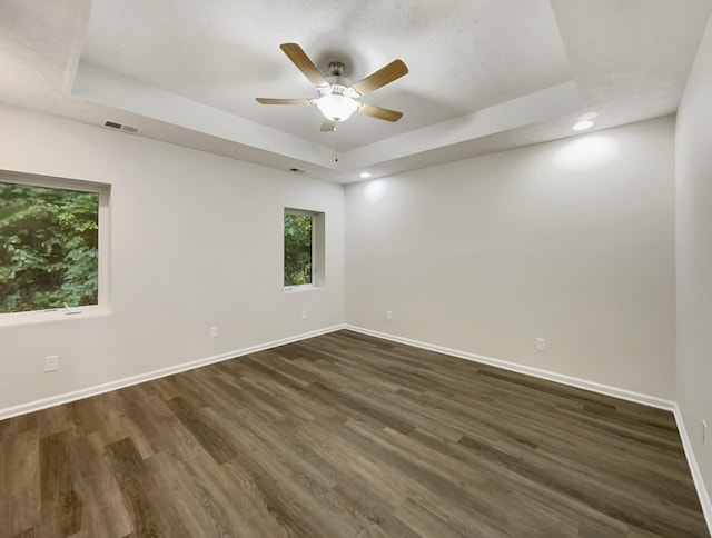 spare room featuring dark wood-style floors, a raised ceiling, visible vents, and baseboards