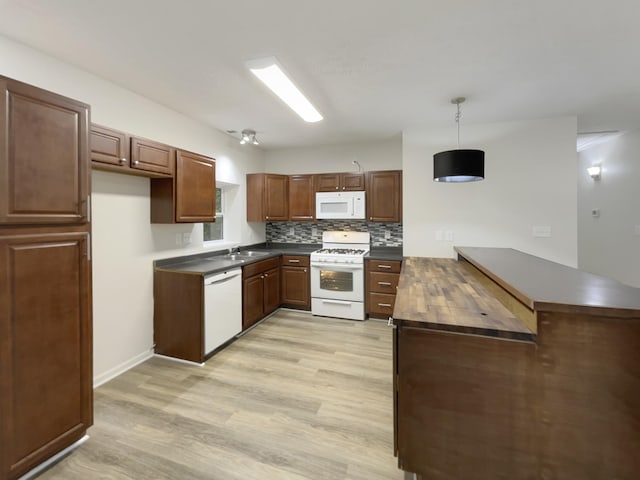 kitchen with a peninsula, white appliances, backsplash, and light wood-style flooring