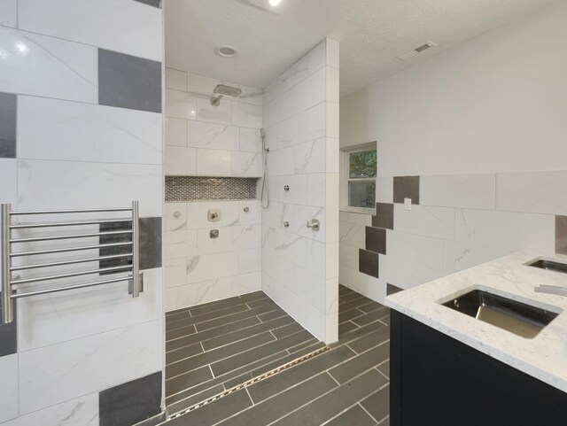 full bathroom featuring a sink, visible vents, tile walls, tiled shower, and radiator heating unit