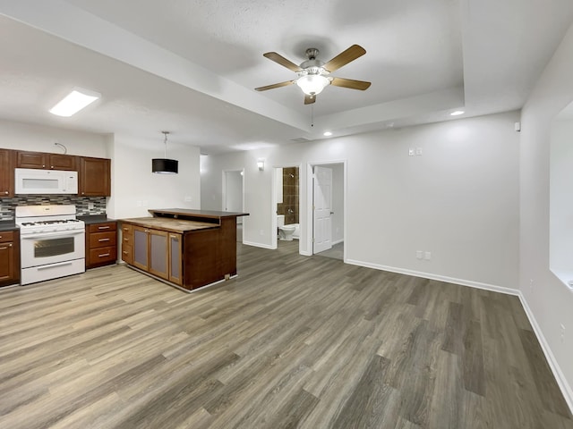 kitchen with a peninsula, white appliances, baseboards, a tray ceiling, and light wood finished floors