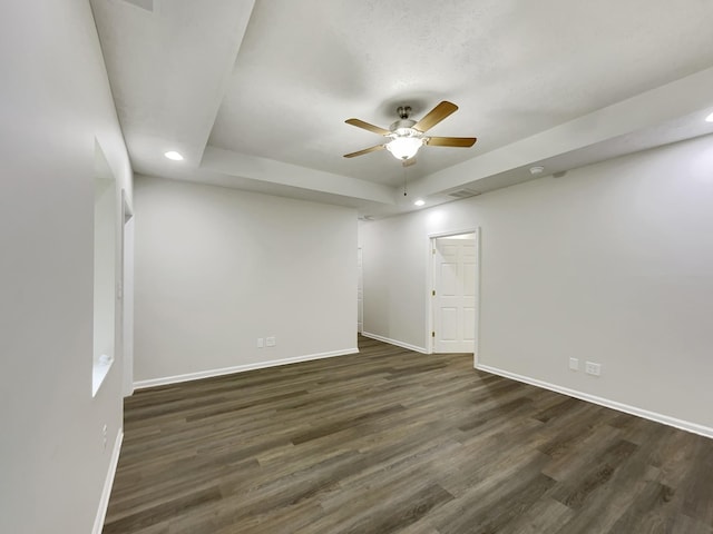 spare room featuring dark wood-type flooring, recessed lighting, a raised ceiling, and baseboards