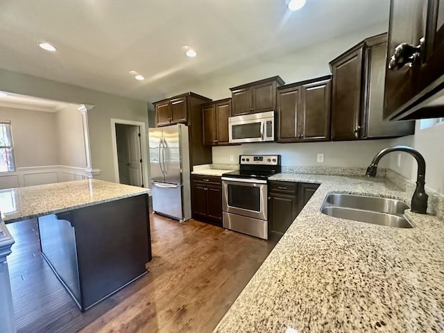 kitchen with dark brown cabinetry, light stone countertops, sink, stainless steel appliances, and a breakfast bar