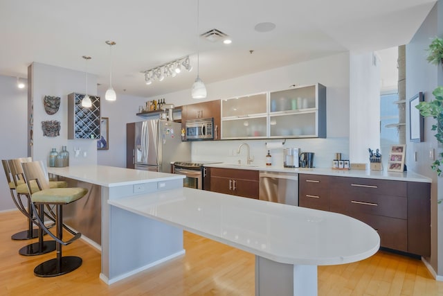 kitchen with appliances with stainless steel finishes, a breakfast bar area, light hardwood / wood-style flooring, dark brown cabinets, and a kitchen island