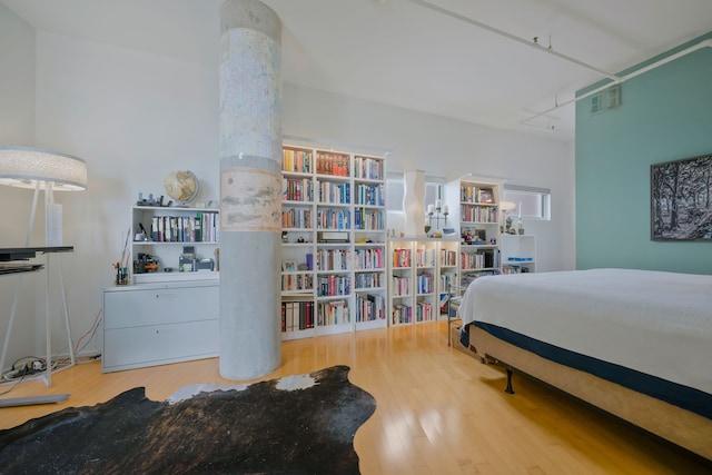 bedroom with decorative columns, light wood-type flooring, and track lighting