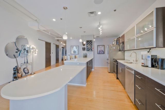 kitchen featuring decorative backsplash, pendant lighting, a center island, appliances with stainless steel finishes, and light hardwood / wood-style flooring