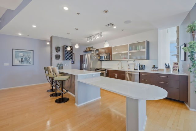 kitchen with a breakfast bar, dark brown cabinets, light wood-type flooring, a kitchen island, and stainless steel appliances