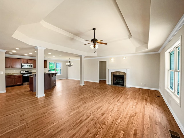 unfurnished living room featuring a tile fireplace, ceiling fan with notable chandelier, ornamental molding, a tray ceiling, and wood-type flooring