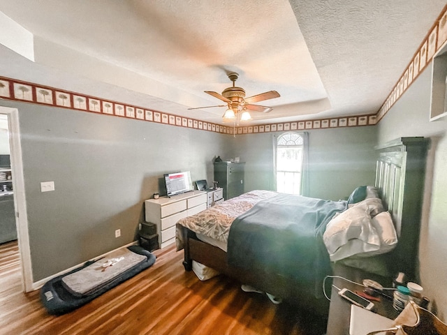 bedroom with a textured ceiling, ceiling fan, a raised ceiling, and wood-type flooring