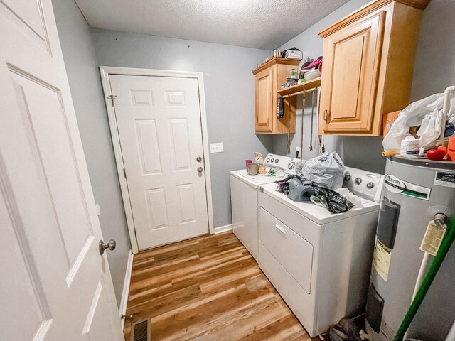 laundry room featuring a textured ceiling, washing machine and dryer, water heater, cabinets, and light hardwood / wood-style floors