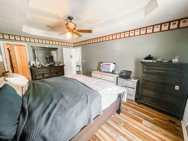 bedroom featuring ceiling fan, a raised ceiling, and light wood-type flooring