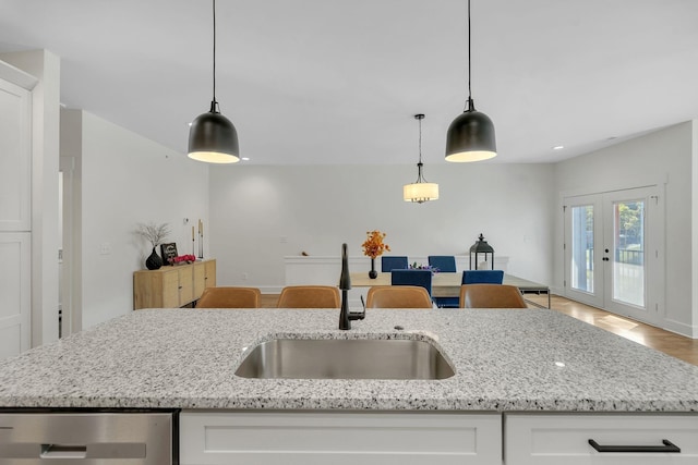 kitchen with an island with sink, white cabinetry, hanging light fixtures, and sink