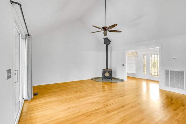 unfurnished living room with a wood stove, vaulted ceiling, light hardwood / wood-style flooring, and ceiling fan