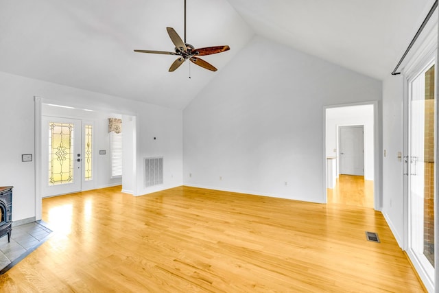 unfurnished living room with light wood-type flooring, high vaulted ceiling, a wood stove, and ceiling fan