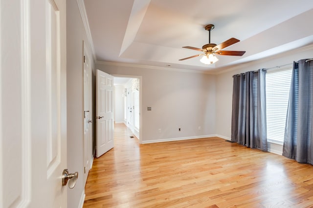 spare room featuring a tray ceiling, ceiling fan, ornamental molding, and light wood-type flooring