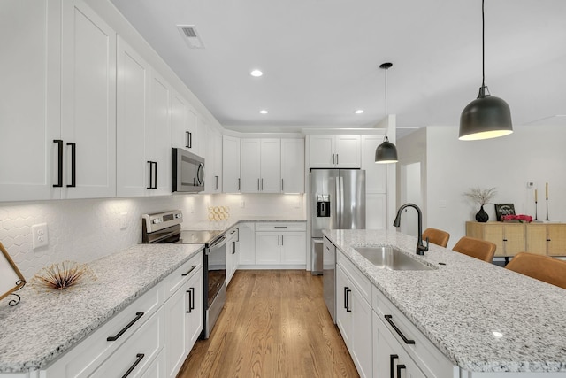 kitchen featuring sink, white cabinetry, stainless steel appliances, an island with sink, and decorative light fixtures