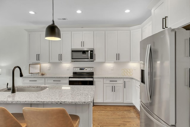 kitchen with appliances with stainless steel finishes, white cabinetry, sink, hanging light fixtures, and light stone counters